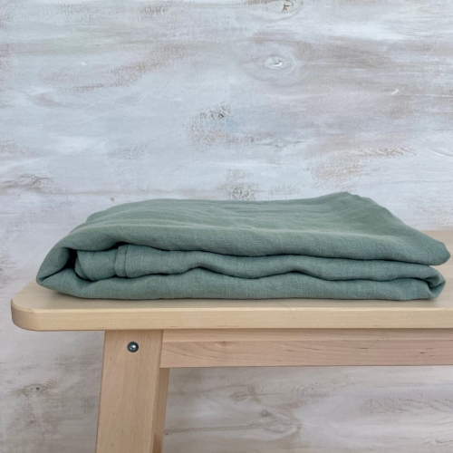 Prześcieradło lniane bez gumki płaskie w kolorze zielonym leży na drewnianej ławie