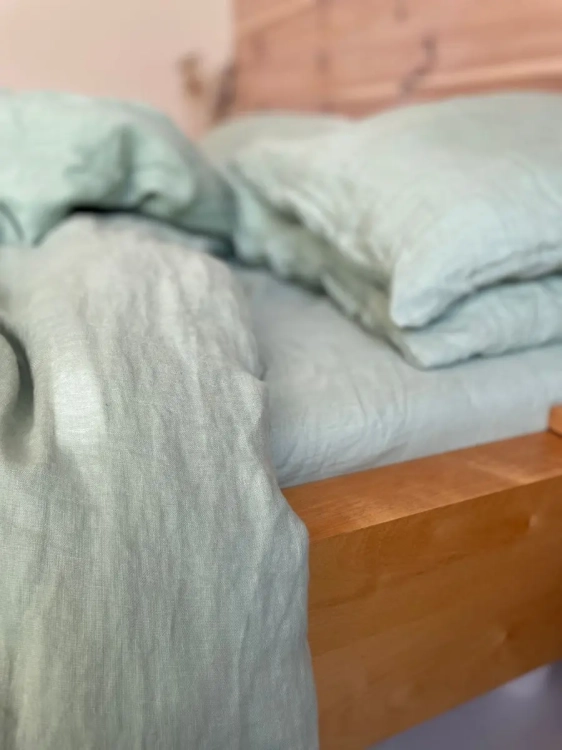 kołdra, poduszki i prześcieradło z lnu w kolorze jasnej szałwiowej zieleni, na drewnianym łóżku