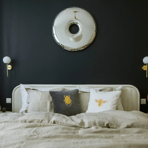 aranżacja łóżka z  lnianą pościelą beżową, ciemnoszarymi i kremowymi poduszkami ozdobnymi z motywami owadów