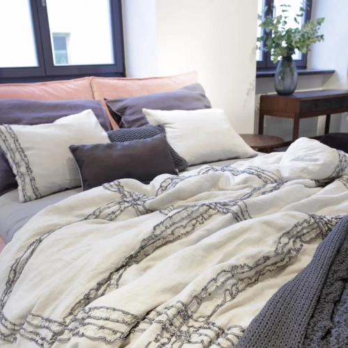 Lniana pościel z falbanką FRILL natural w połączeniu z pościelą grafitową. Fragment łóżka