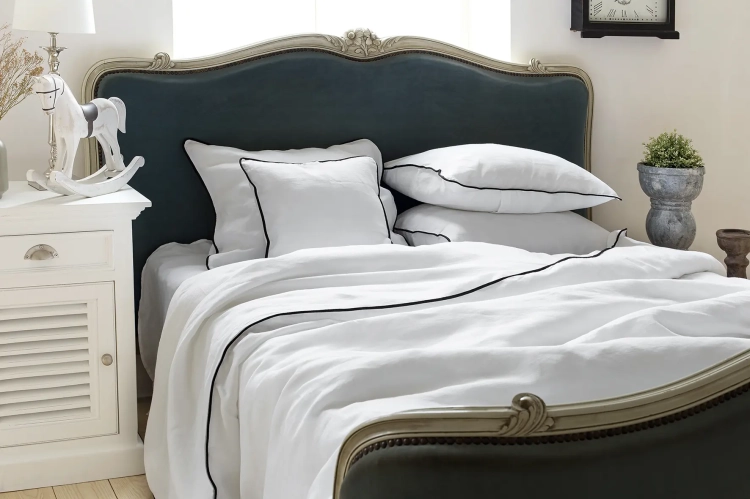 lniana poszewka na poduszkę Black White biała z czarną wypustkąbiała lniana pościel Black White z czarną wypustką na granatowym łóżku ze złotą ramą, widok z boku