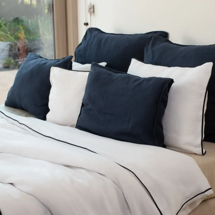 zestawienie białej lnianej pościeli z czarną obramówką, z ciemnymi granatowymi poduszkami