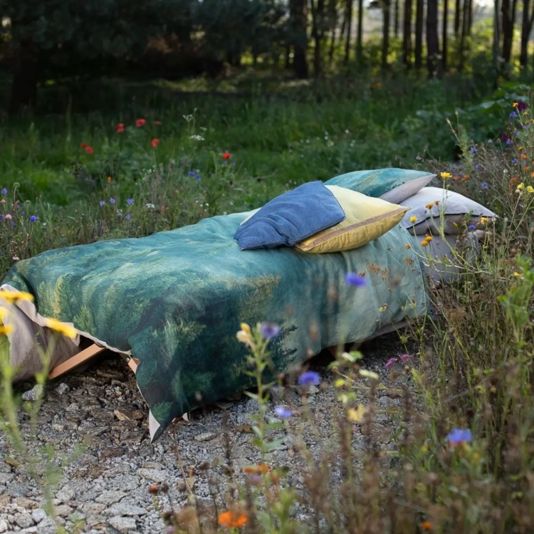 łózko ogrodowe z pościelą z motywem lasu i kolorowymi poduszkami, na tle lasu