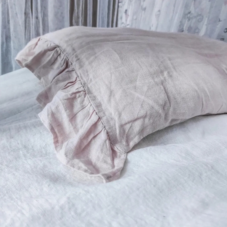 Lniana poszewka na poduszkę z falbankami różowa leży na białym lnianym prześcieradle
