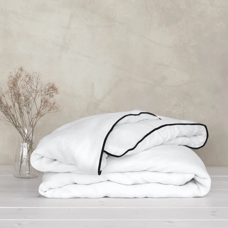 Złożona kołdra w białej lnianej poszewce z czarną wypustką