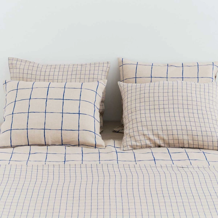 Poduszki lniane GRID w granatową małą i dużą kratę. Fragment łóżka z pościelą