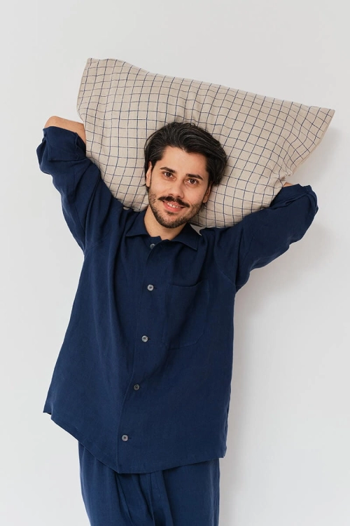 Mężczyzna w granatowej koszuli lnianej trzyma poduszkę w kratę