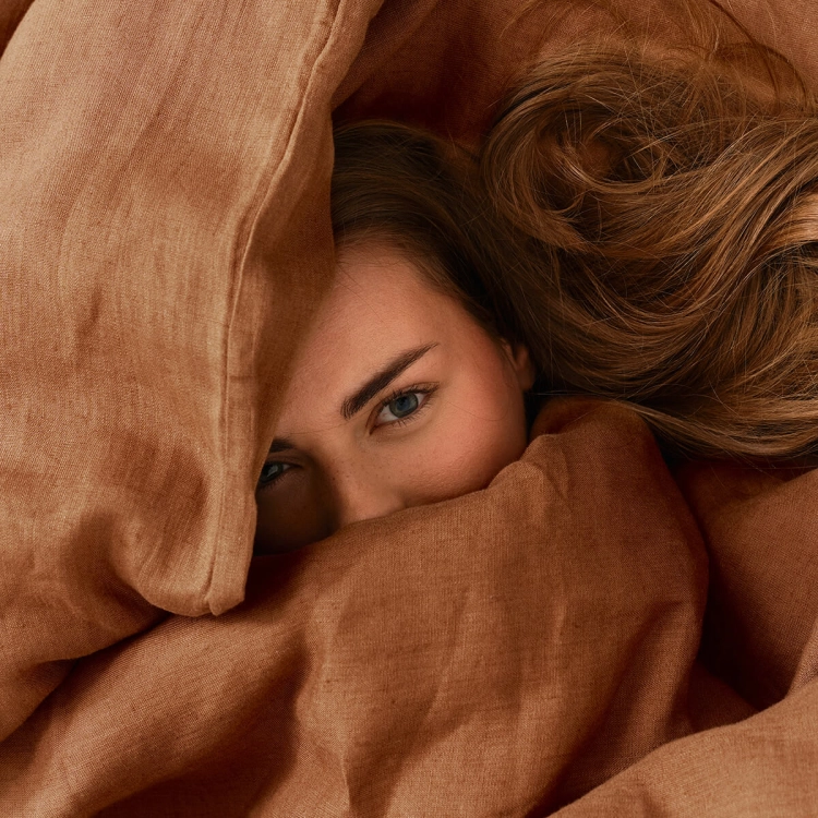 dziewczyna otulona lnianą cynamonową  pościelą