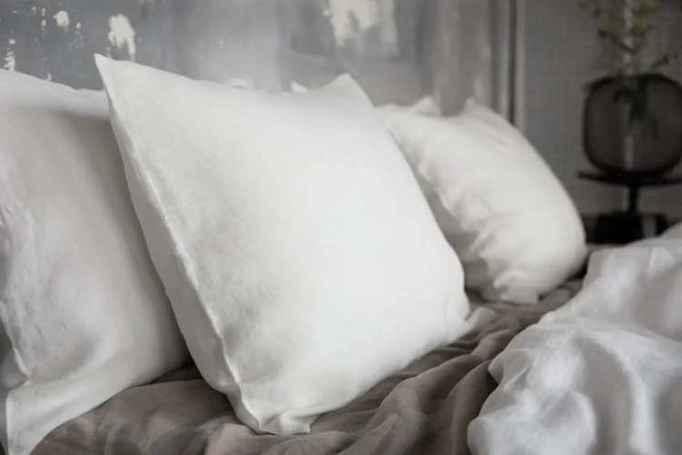 poduszki w lnianych biało kremowych poszewkach. Fragment łóżka