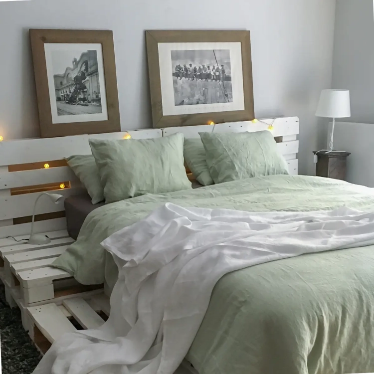 Komplet pościeli lnianej jasnozielonej na łózku z białych palet