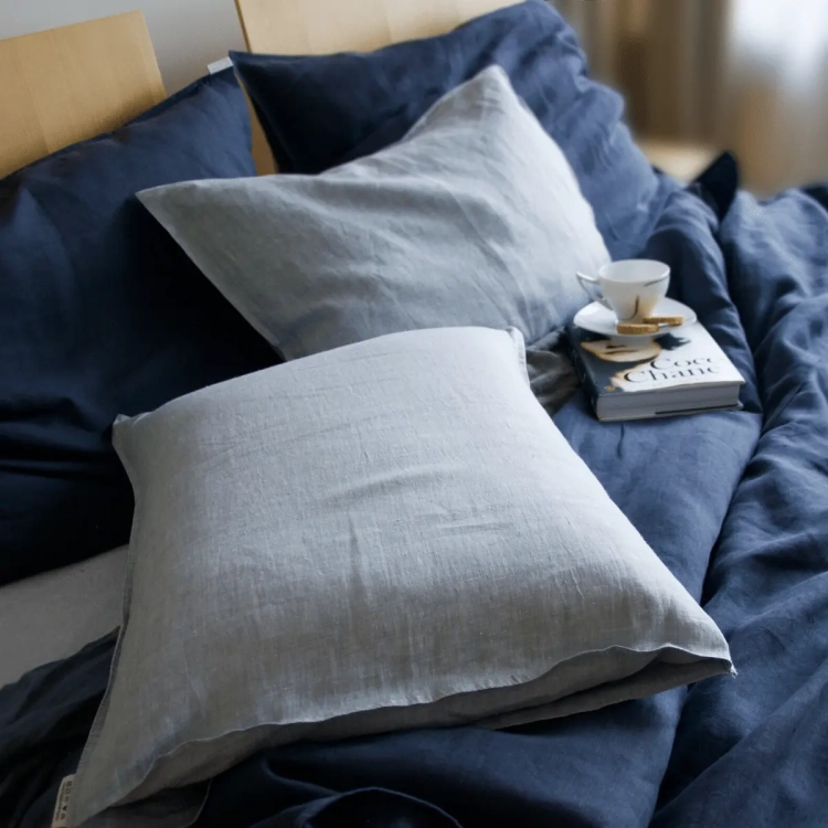 Fragment łózka z lnianą pościelą. Połączenie białych i granatowych poduszek