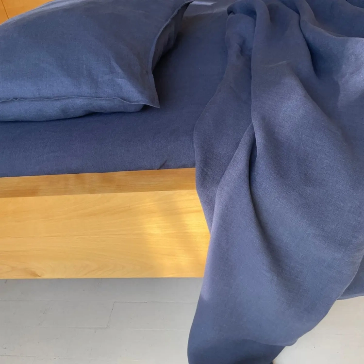 Granatowa pościel lniana BASIC nawy blue. Fragment łóżka ze zwisającym narożnikiem kołdry