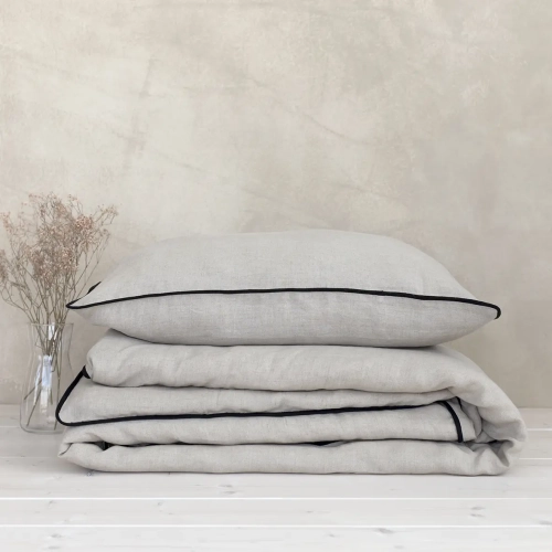 Poduszka leży na złożonej kołdrze. Komplet pościeli lnianej beżowej z czarnym obszyciem